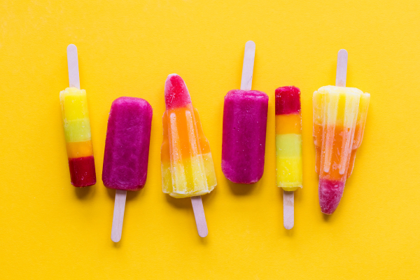 A selection of bright ice lollies on a yellow background