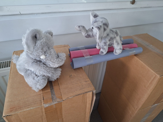 A stable paper tube bridge across the gap between two boxes being tested with an elephant toy on top of it.