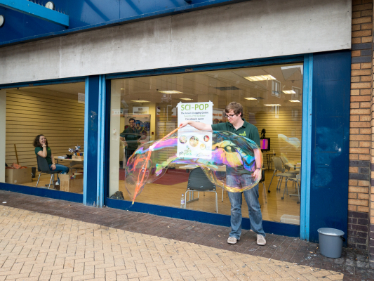 NUSTEM staff outside a pop-up shop in a shopping centre, blowing giant soap bubbles